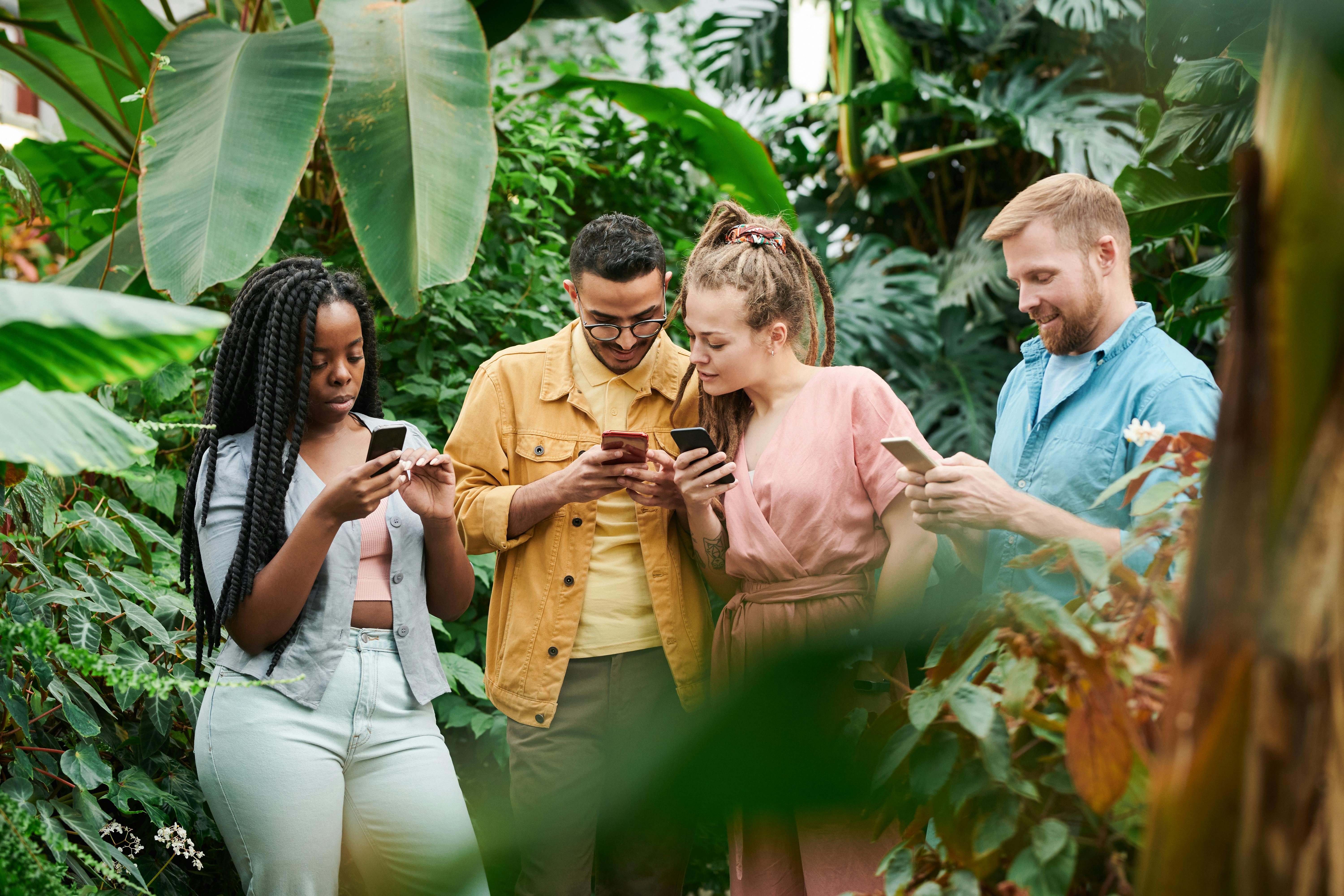 Group of friends using phones together in natural botanical setting